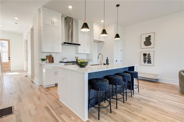 kitchen with white cabinetry, wall chimney exhaust hood, a center island with sink, and sink