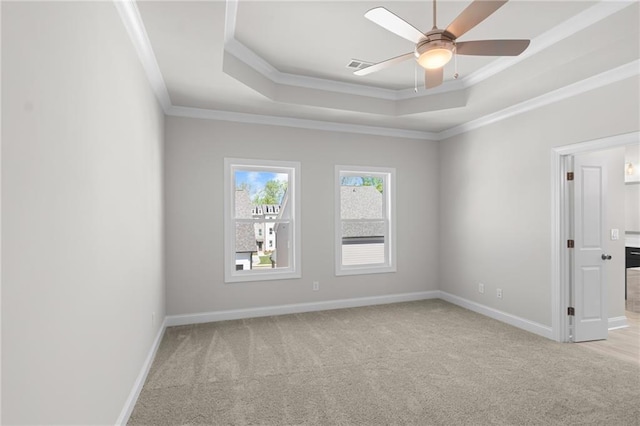 empty room featuring a ceiling fan, baseboards, a tray ceiling, crown molding, and light colored carpet