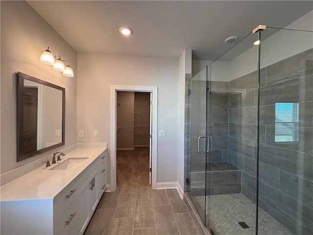 full bathroom featuring baseboards, a spacious closet, a stall shower, and vanity