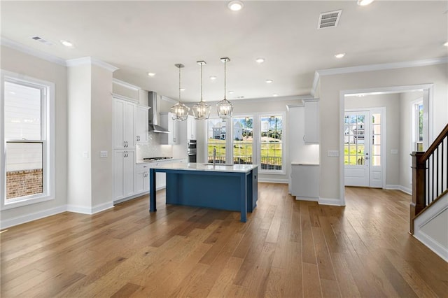 kitchen featuring visible vents, backsplash, light wood-style floors, and wall chimney range hood