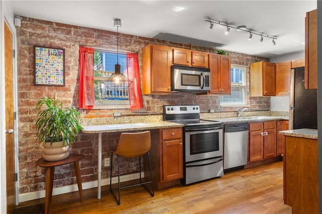 kitchen featuring a kitchen bar, decorative light fixtures, light wood-type flooring, appliances with stainless steel finishes, and light stone countertops