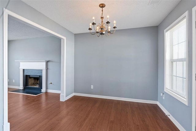 unfurnished dining area with wood-type flooring, a chandelier, and a textured ceiling