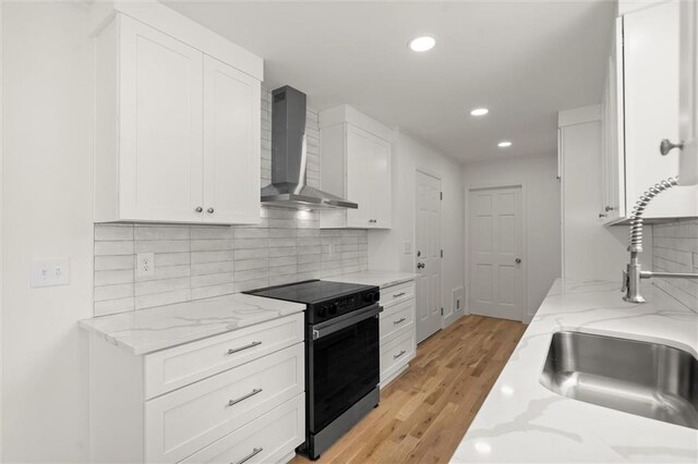 kitchen with electric range, light wood finished floors, wall chimney exhaust hood, recessed lighting, and white cabinetry