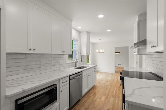 kitchen with a sink, appliances with stainless steel finishes, an inviting chandelier, and white cabinetry
