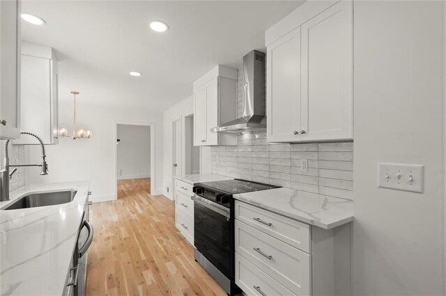 kitchen featuring decorative backsplash, electric stove, wall chimney exhaust hood, white cabinetry, and a sink