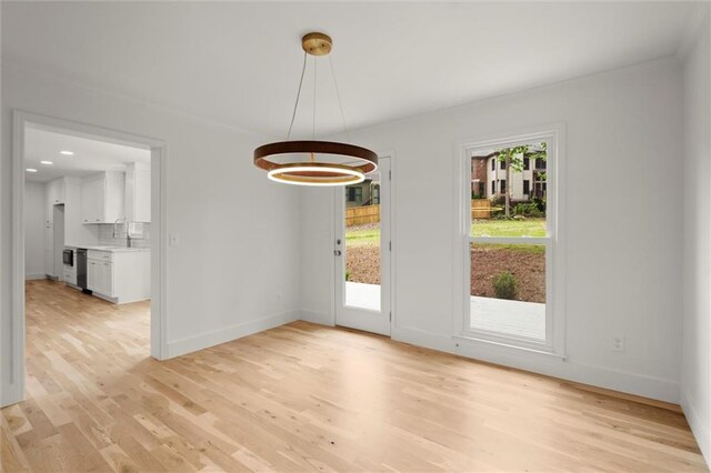 unfurnished dining area with baseboards, a notable chandelier, a sink, and light wood-type flooring