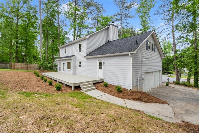 back of property with driveway, a chimney, a wooden deck, fence, and an attached garage