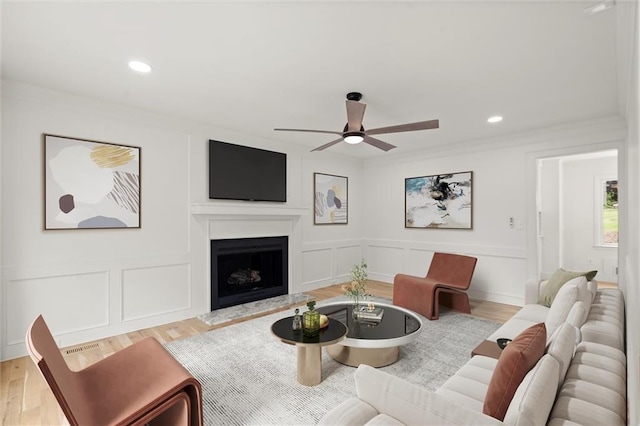 living room featuring ceiling fan, a fireplace with raised hearth, a decorative wall, and wood finished floors