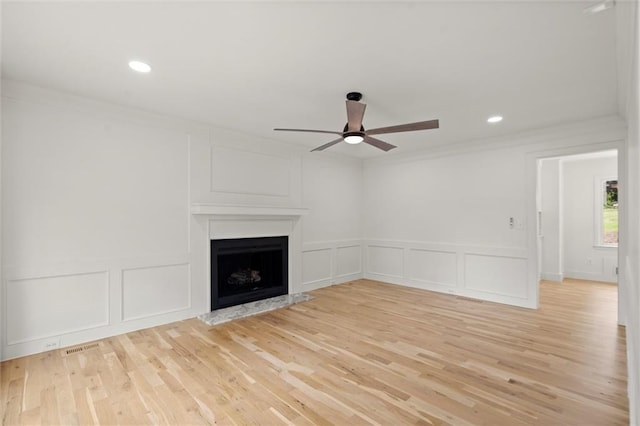 unfurnished living room with a fireplace with raised hearth, ceiling fan, ornamental molding, and a decorative wall