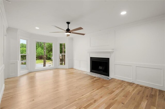 unfurnished living room with visible vents, a decorative wall, a fireplace with raised hearth, a ceiling fan, and light wood-style flooring