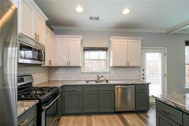 kitchen featuring hanging light fixtures, green cabinetry, white cabinetry, appliances with stainless steel finishes, and sink