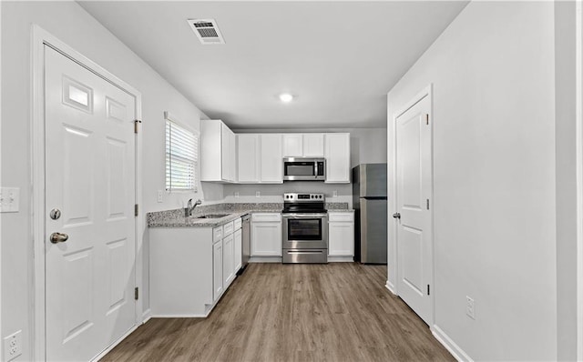 kitchen with sink, light stone counters, white cabinetry, light hardwood / wood-style floors, and stainless steel appliances