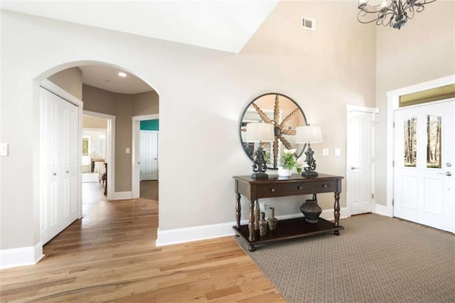 corridor with visible vents, wood finished floors, arched walkways, baseboards, and a towering ceiling