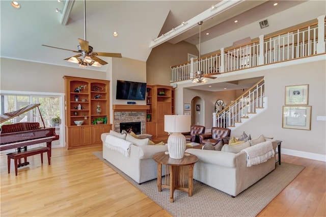 living room with baseboards, a ceiling fan, a fireplace, stairway, and light wood-style flooring