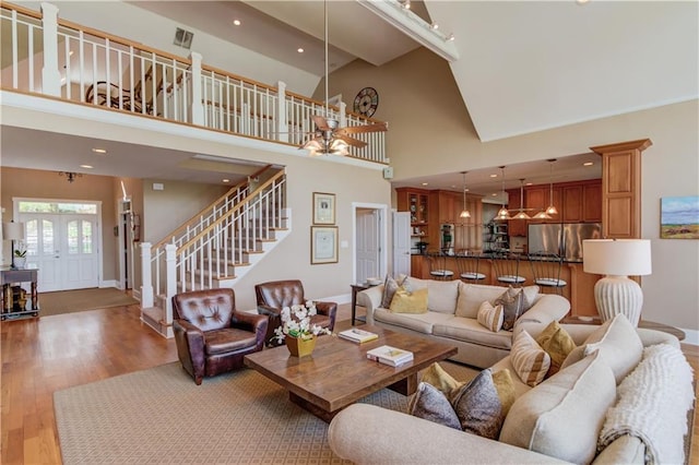 living room featuring baseboards, a high ceiling, a chandelier, wood finished floors, and stairs