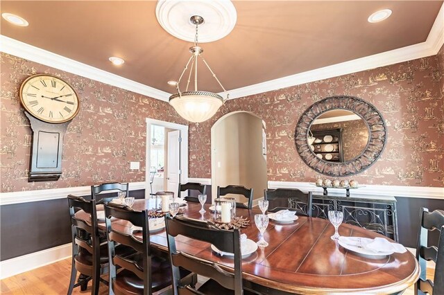 dining space with wallpapered walls, wood finished floors, ornamental molding, and wainscoting