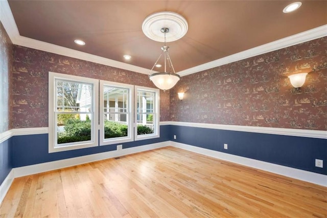 empty room featuring a wainscoted wall, wallpapered walls, crown molding, and wood finished floors