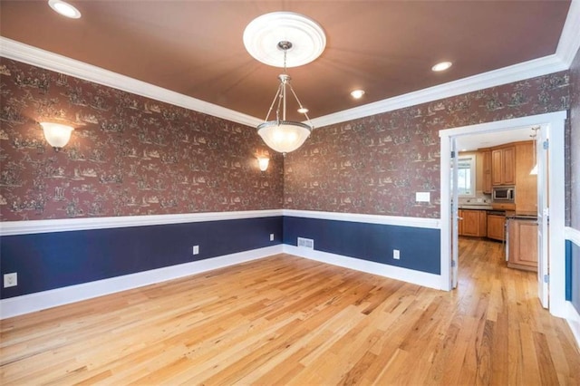 spare room featuring baseboards, light wood finished floors, wallpapered walls, wainscoting, and crown molding