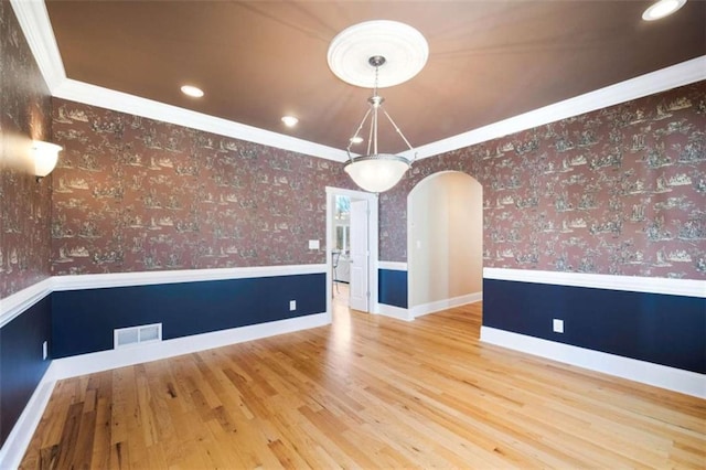 unfurnished dining area featuring arched walkways, a wainscoted wall, and wallpapered walls