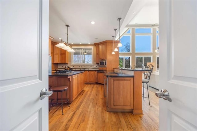 kitchen featuring dark countertops, a peninsula, stainless steel microwave, a kitchen breakfast bar, and brown cabinets