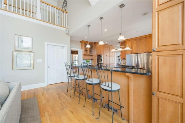 kitchen with baseboards, light wood finished floors, stainless steel appliances, a kitchen breakfast bar, and decorative light fixtures