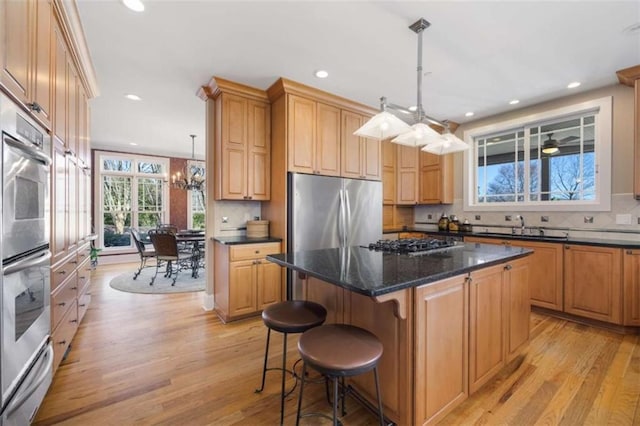 kitchen featuring light wood finished floors, a center island, decorative backsplash, appliances with stainless steel finishes, and a sink