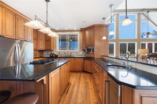 kitchen featuring light wood-type flooring, brown cabinets, a sink, a kitchen island, and appliances with stainless steel finishes