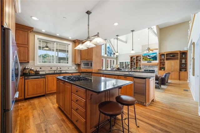 kitchen featuring a center island, appliances with stainless steel finishes, a peninsula, brown cabinetry, and light wood finished floors