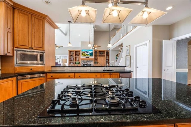 kitchen with dark stone countertops, brown cabinetry, a sink, stainless steel microwave, and black gas stovetop