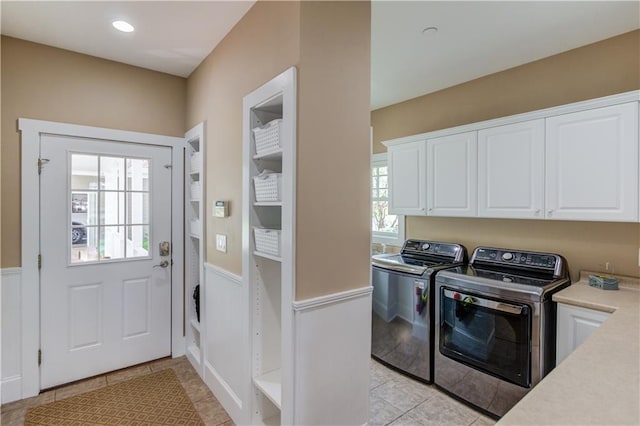 laundry area featuring light tile patterned floors, wainscoting, washing machine and clothes dryer, and cabinet space