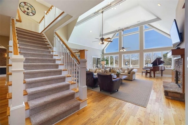 living area with high vaulted ceiling, hardwood / wood-style floors, stairway, a stone fireplace, and baseboards