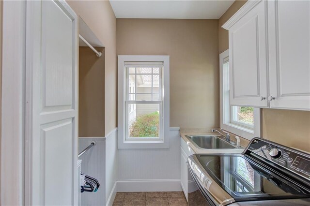 washroom with baseboards, wainscoting, cabinet space, washer and dryer, and a sink