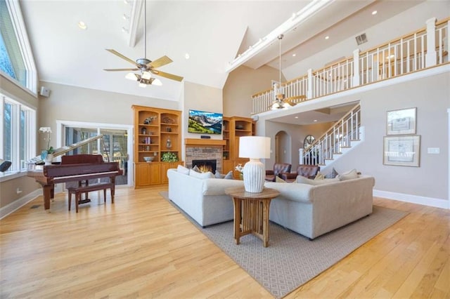 living room with baseboards, stairs, light wood-type flooring, a fireplace, and high vaulted ceiling