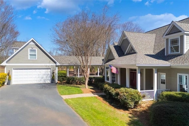 view of front of property featuring a front lawn, driveway, covered porch, roof with shingles, and a garage