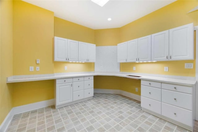 kitchen with white cabinetry, light countertops, baseboards, and built in study area