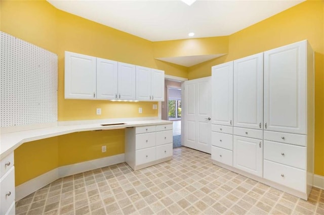 kitchen featuring light countertops, white cabinets, baseboards, and built in study area