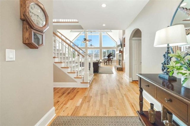 corridor featuring arched walkways, light wood finished floors, stairs, and baseboards