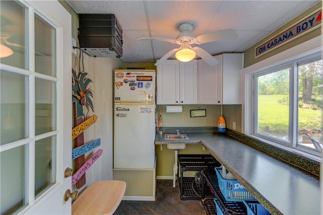 kitchen with baseboards, white cabinets, stone finish floor, ceiling fan, and a sink
