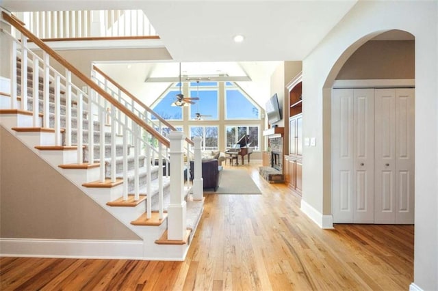 entrance foyer with a ceiling fan, wood finished floors, baseboards, a fireplace, and a towering ceiling