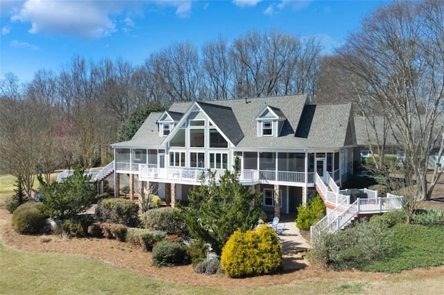 rear view of property featuring stairway, a shingled roof, and a sunroom