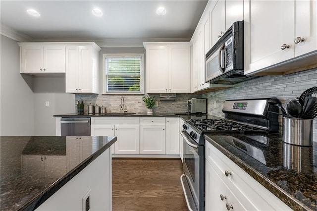 kitchen with appliances with stainless steel finishes, white cabinetry, dark stone countertops, crown molding, and sink