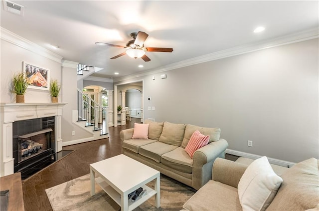 living room with decorative columns, a tiled fireplace, ornamental molding, and dark hardwood / wood-style floors