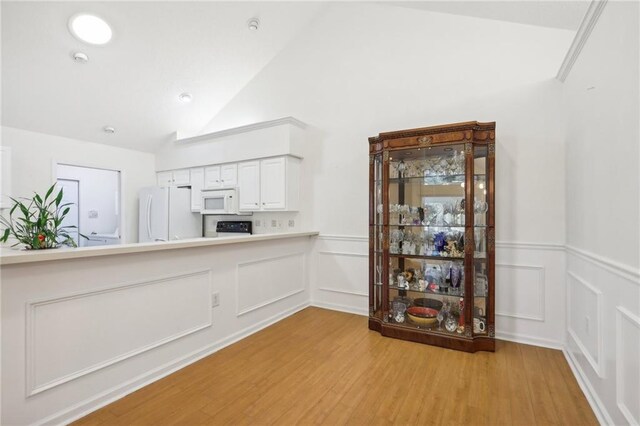 kitchen with white cabinets, light hardwood / wood-style floors, white appliances, and high vaulted ceiling