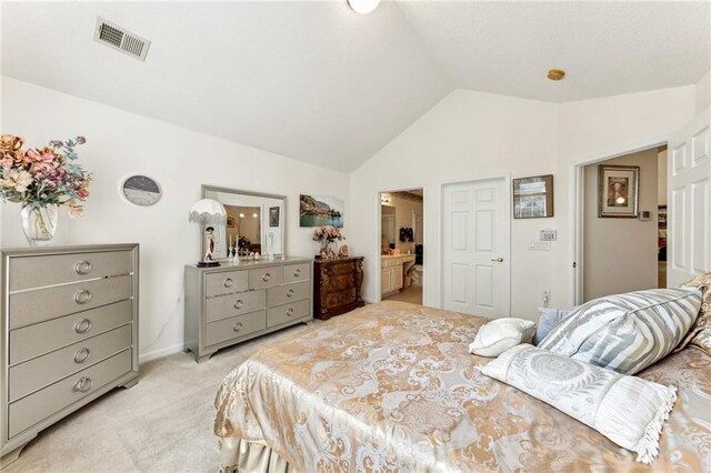 bedroom with light colored carpet, lofted ceiling, and ensuite bath