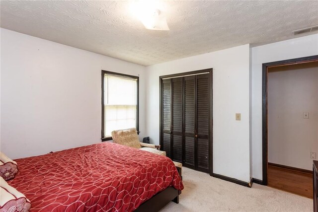bedroom featuring a textured ceiling, visible vents, baseboards, a closet, and light carpet