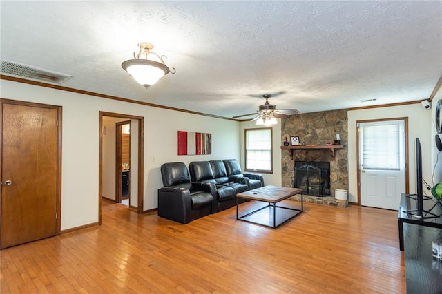 living area with visible vents, ornamental molding, light wood-style floors, a textured ceiling, and a ceiling fan