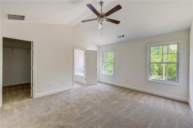 unfurnished bedroom with connected bathroom, lofted ceiling, a walk in closet, ceiling fan, and light carpet