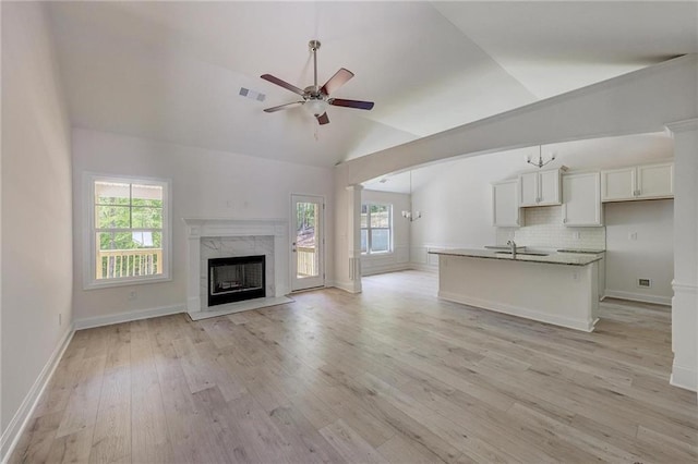 unfurnished living room featuring ceiling fan, a wealth of natural light, vaulted ceiling, and light wood-type flooring