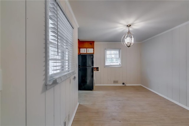 unfurnished dining area with a notable chandelier, ornamental molding, and light wood-type flooring