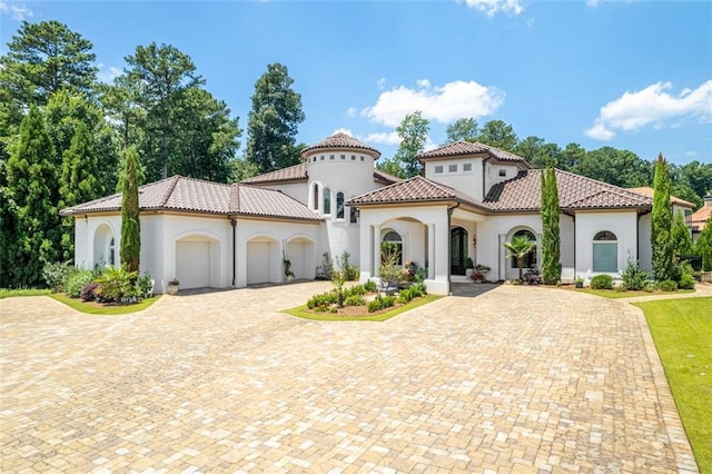 mediterranean / spanish home with a tiled roof, an attached garage, driveway, and stucco siding